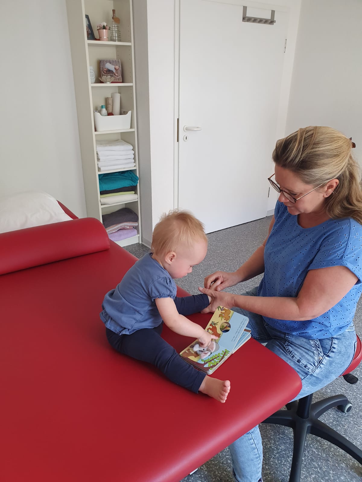 Kerstin Nieger führt mit einem Kleinkind auf der Therapieliege eine spielerische Handlungsanleitung durch – Teil ihrer Bobath- oder Vojta-Therapie zur Förderung der motorischen Entwicklung.