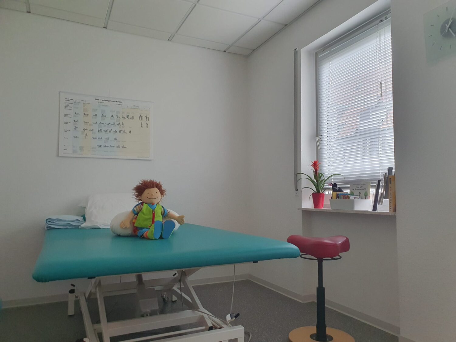 Behandlungsraum mit Liege, Kindertherapie-Puppe und heller Fensterfront in der Praxis für Physiotherapie Kerstin Nieger.